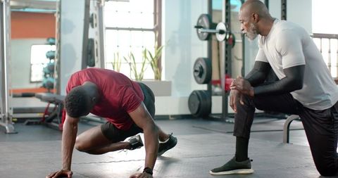 Personal trainer coaching athlete performing plank variation for core strength in gym