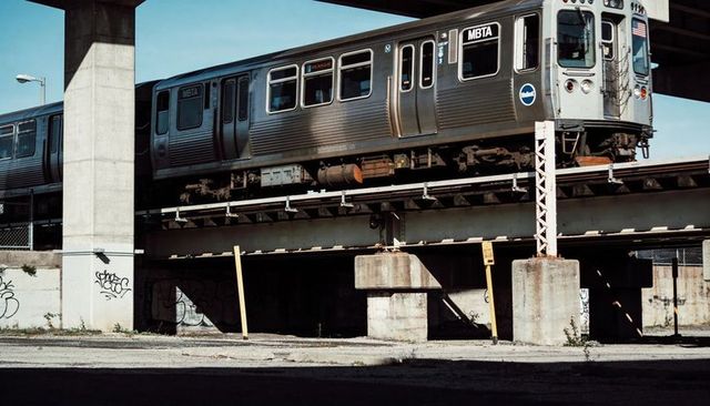 MBTA Stainless-Steel Train Traveling on Elevated Tracks Above Industrial Lot