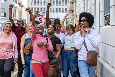 Diverse friends taking selfie while walking through city street, celebrating together
