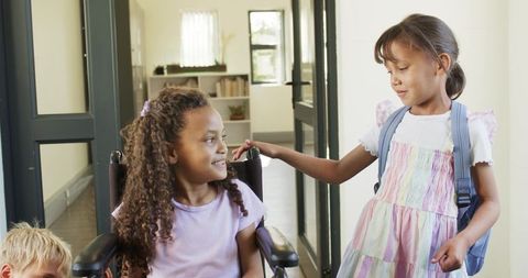 Inclusive school friendship smiling classmates helping child in wheelchair at corridor doorway