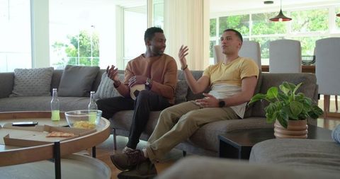 Diverse friends relaxing and chatting on sofa with pizza, drinks and soccer ball