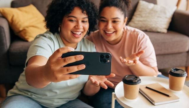 Two friends taking selfie on couch with coffee cups and notebook cozy home lifestyle
