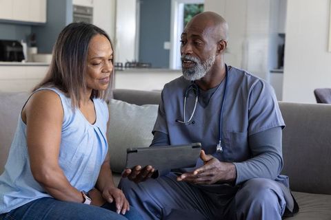 African american male nurse consulting woman at home with tablet during healthcare visit
