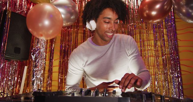 Image of happy african american male dj playing music, dancing and making gestures at a nightclub. Fun, inclusivity, going out and party concept.
