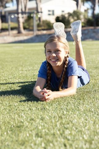 Smiling girl with braids lying on green grass wearing blue shirt white sneakers outdoors