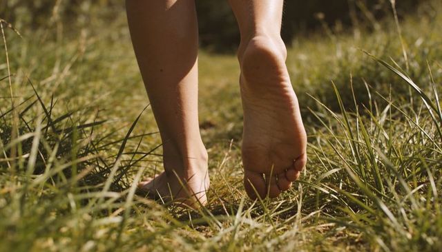 Walking barefoot along sunlit meadow path close-up of soles pressing through grass