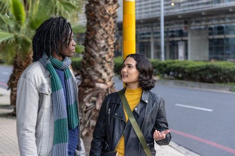 Multicultural friends talking on urban palm-lined sidewalk with tablet and winter scarves
