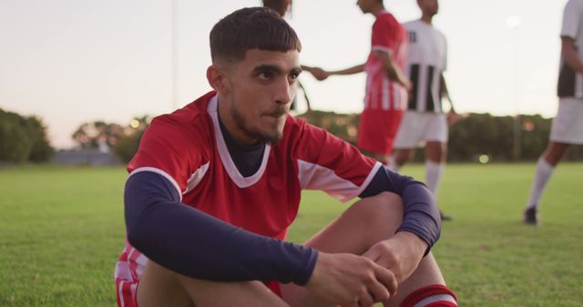 Young soccer player sitting from a challenging match, fielding competition of a game outdoors. Ideal for sports-related content, inspirational stories, teamwork and athletic dedication.