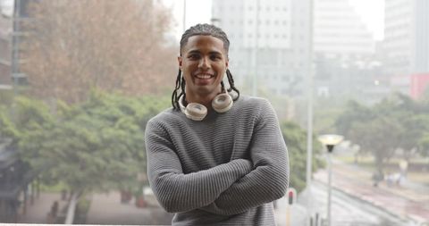 Confident African American Man Standing on Balcony Wearing Headphones Overlooking Misty Urban Plaza