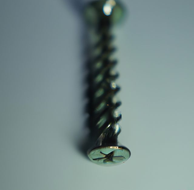 Close-up of a metal screw lying on a smooth, light-colored surface. Shallow depth of field focuses on the head and threading of the screw, emphasizing its detailed design. Ideal for use in articles or advertisements related to hardware, construction, tools, and DIY projects.