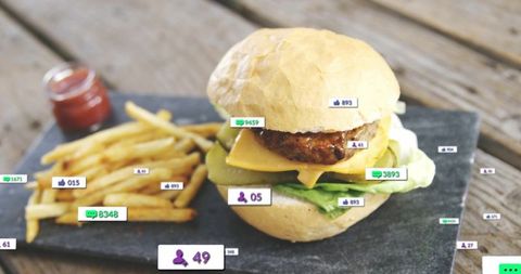 Juicy cheeseburger with fries and social media engagement icons on rustic wooden table