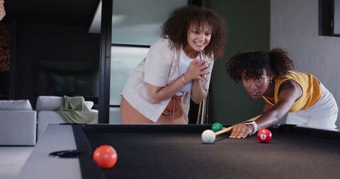 African american friends playing pool in contemporary apartment laughing and concentrating