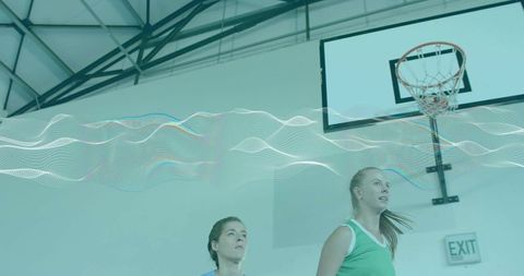 Women Basketball Players Gazing Up at Hoop with Abstract Digital Wave Overlay on Gym Court