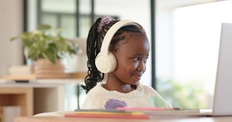 African American girl wearing headphones learning on laptop in bright home workspace