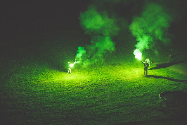 Two People Holding Green Smoke Flares at Night on Grass Field - Download Free Stock Photos Pikwizard.com