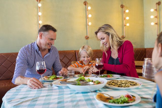 This image showcases a happy family enjoying dinner together at a restaurant. It can be used for advertisements promoting family-friendly restaurants, dining out experiences, or family bonding activities. Perfect for websites, brochures, and social media posts targeting family dining and lifestyle content.