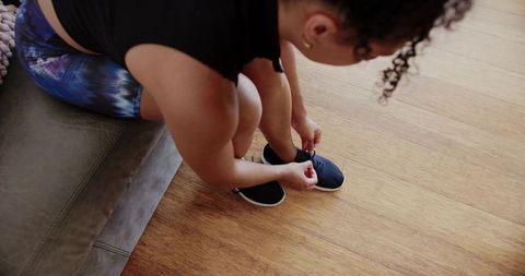 African american woman tying sneakers on couch preparing for workout