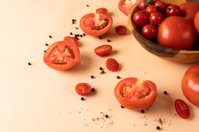 This image showcases fresh tomatoes, both whole and sliced, along with peppercorn and salt on a pink background. Ideal for use in culinary blogs, healthy eating articles, organic food promotions, and vegetarian or vegan recipe websites. The vibrant colors and natural presentation make it perfect for marketing materials related to fresh produce and healthy lifestyles.