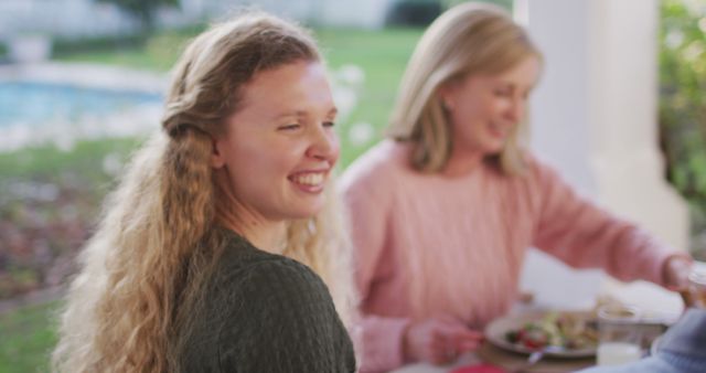 Image of happy caucasian mother and grandmother laughing at outdoor family dinner table. Family, domestic life and togetherness concept digitally generated image.