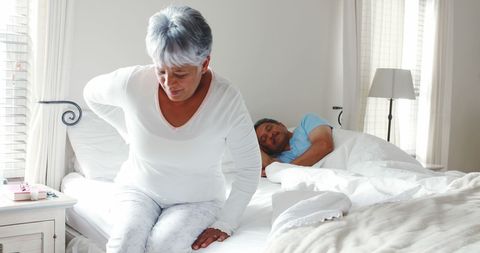 Middle-Aged Woman with Back Pain in Bedroom, Restless Partner