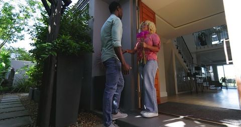 Man Presenting Flowers to Woman at Home Entrance with Bright Smile