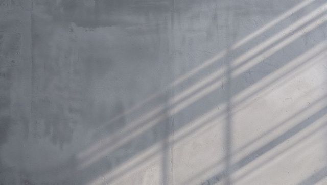 Casting diagonal window-grid shadows on textured plaster wall, minimal concrete interior