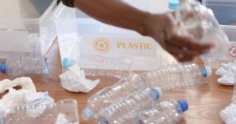 African american man reaching and sorting plastic bottles for recycling on wooden table