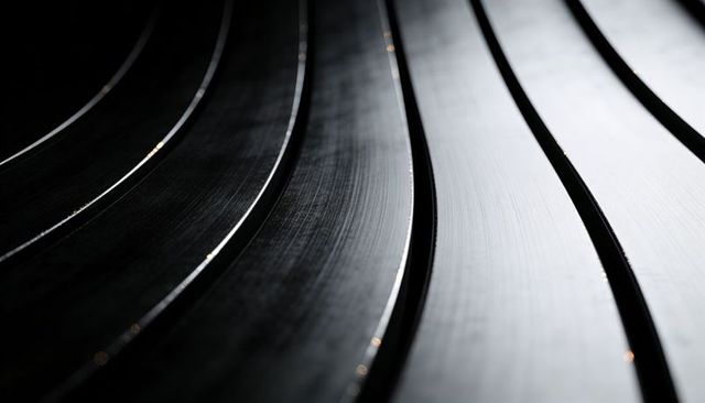 Curving metallic grooves catching low-angle highlights and dark channels, monochrome