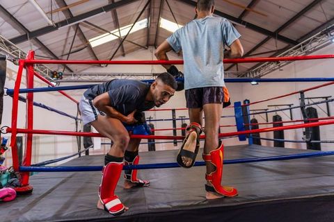 African american fighters adjusting shin guards and preparing for sparring in boxing ring