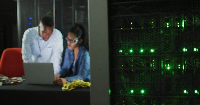 IT professionals working with laptop next to server rack with green lights - Download Free Stock Images Pikwizard.com