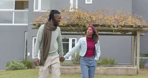 Diverse Couple Walking Hand in Hand Through Urban Courtyard in Casual Autumn Fashion