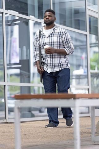 African american commuter walking with coffee and bag outside modern glass building
