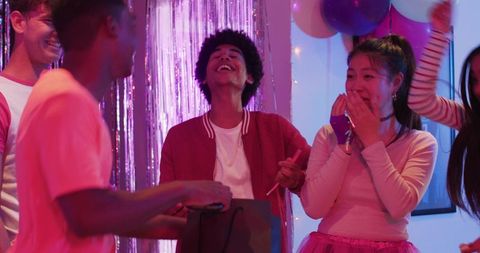 Diverse Friends Laughing and Exchanging Gift at Colorful Neon Birthday Party with Balloons