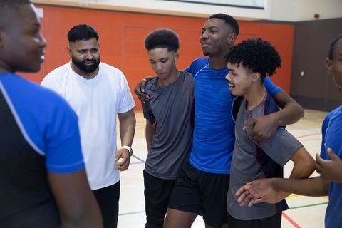 African american teen basketball team huddling with coach in gymnasium showing teamwork