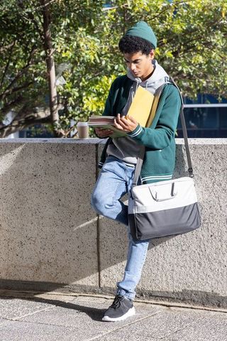 College student studying on campus wall with coffee, notebooks and shoulder bag