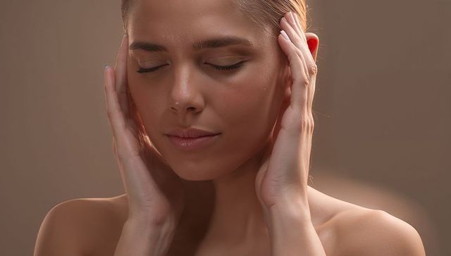 Serene woman cupping face with hands relaxing under soft warm lighting skincare portrait