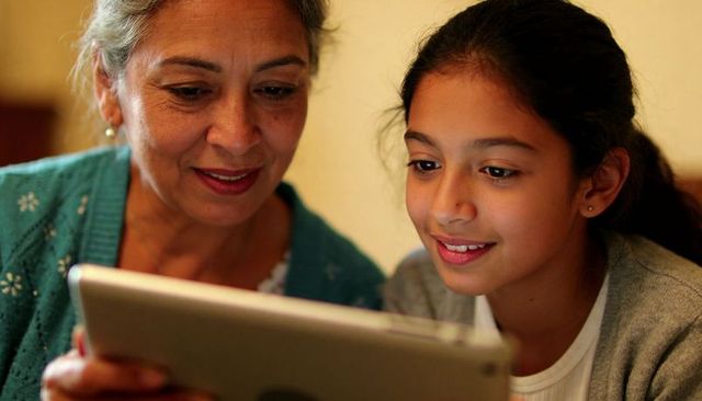 Senior woman and teen girl sharing tablet, learning together in multigenerational home