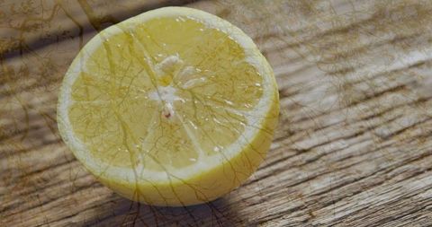 Fresh halved lemon with rustic twig shadows on wooden surface