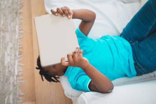 African american boy lying on couch using tablet. at home in isolation during quarantine lockdown.