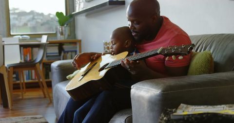 Father Teaching Son Guitar on Cozy Home Sofa