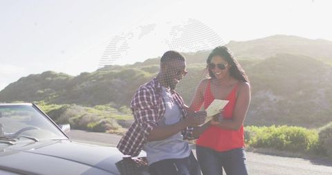 Couple reading map beside convertible on coastal road, enjoying sunny spontaneous road trip