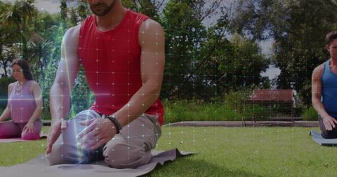 Kneeling man meditating on yoga mat in park with bracelet and group