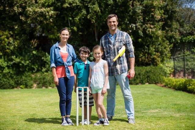 Family enjoying a game of cricket in a park on a sunny day. Parents and children bonding through outdoor activities. Perfect for advertisements promoting family time, outdoor recreation, and healthy lifestyles.