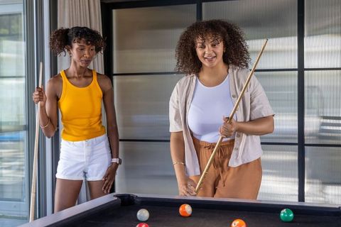 Diverse friends playing pool in modern lounge holding cue sticks and smiling