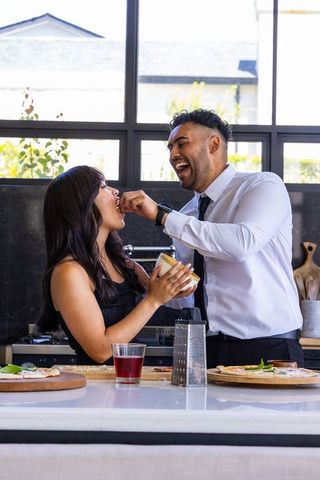 Sunlit modern kitchen couple feeding each other while preparing homemade margherita pizza
