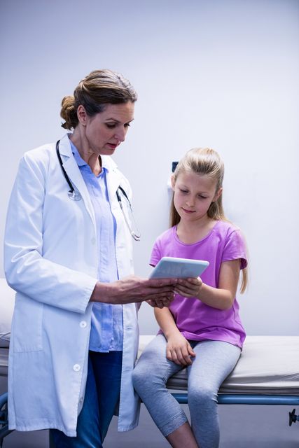 Doctor showing medical report to young patient on tablet in hospital. Ideal for use in healthcare, medical technology, pediatric care, and patient education materials.
