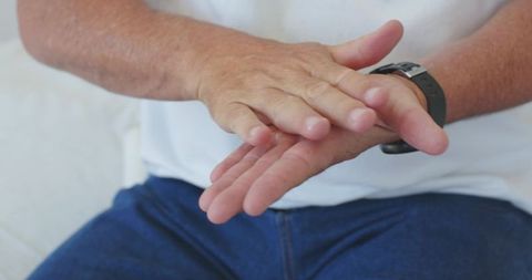 Mature man resting hands on lap wearing wristwatch and casual denim outfit close-up