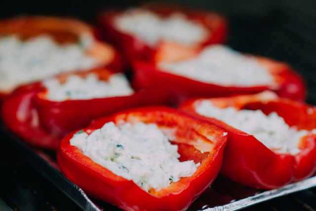 Grilled red bell peppers stuffed with a creamy cheese filling are arranged on a metal tray, ready for a delicious meal. Perfect to use in content focused on healthy eating, summer grilling, vegetarian recipes, or gourmet cooking. Ideal for food blogs, cooking magazines, or recipe websites.