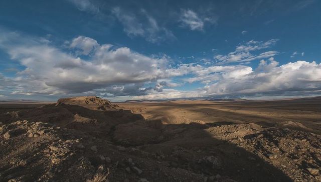 Expansive semi-arid plateau revealing rounded mesa, rocky foreground and cloud shadows