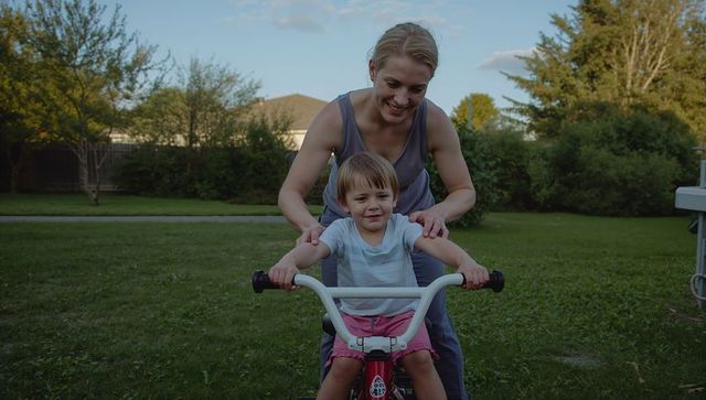 Woman steadying smiling child learning to ride bicycle in suburban backyard